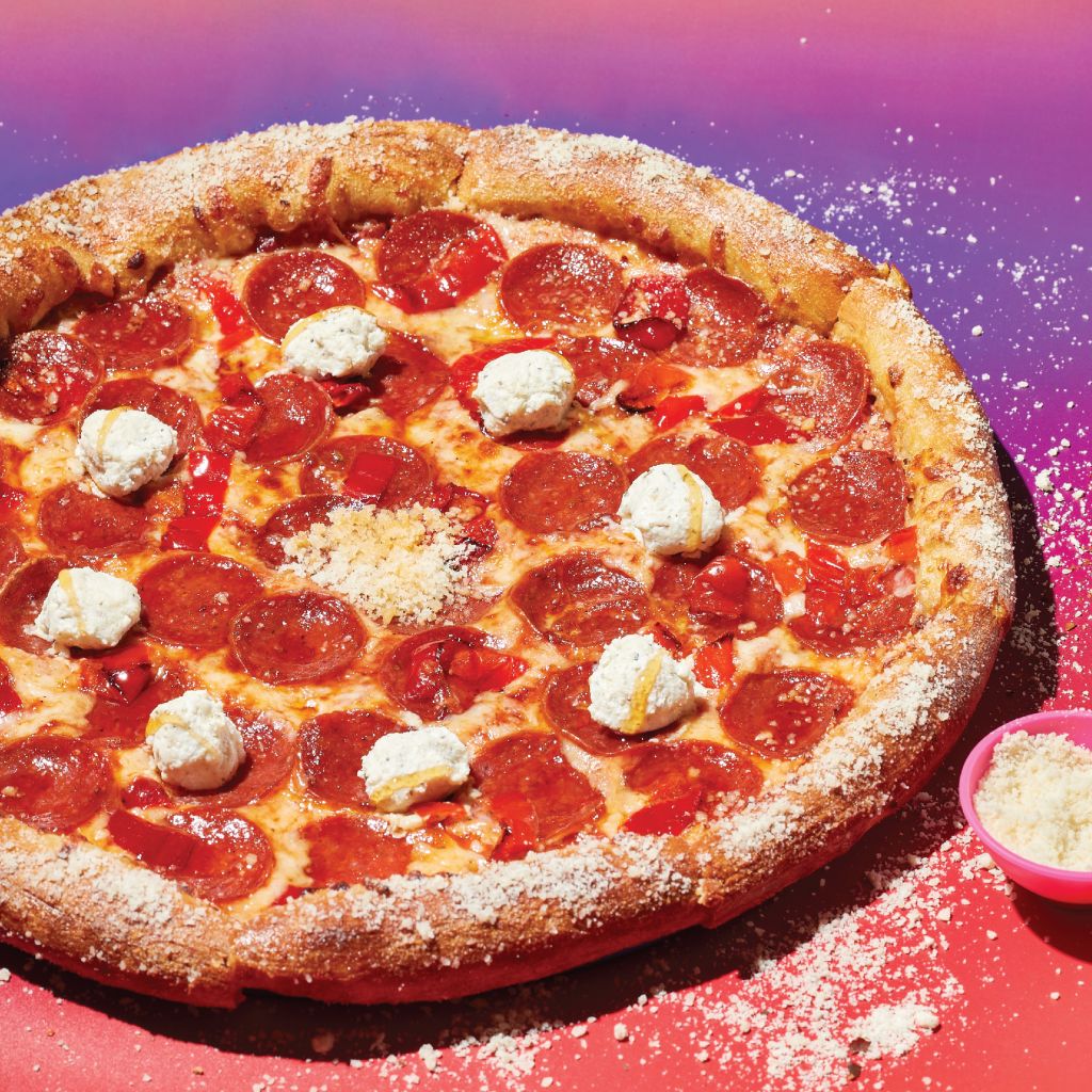 A large pepperoni pizza with white cheese dots and red peppers on a colorful background in Atlanta, Georgia.