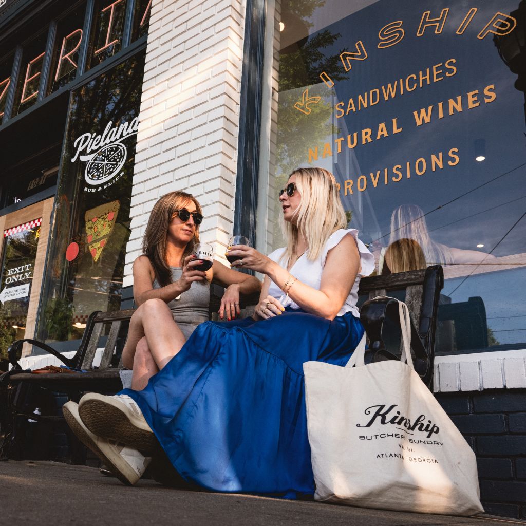 Two women enjoying wine on a bench outside a restaurant with a blue awning in Atlanta, Georgia.