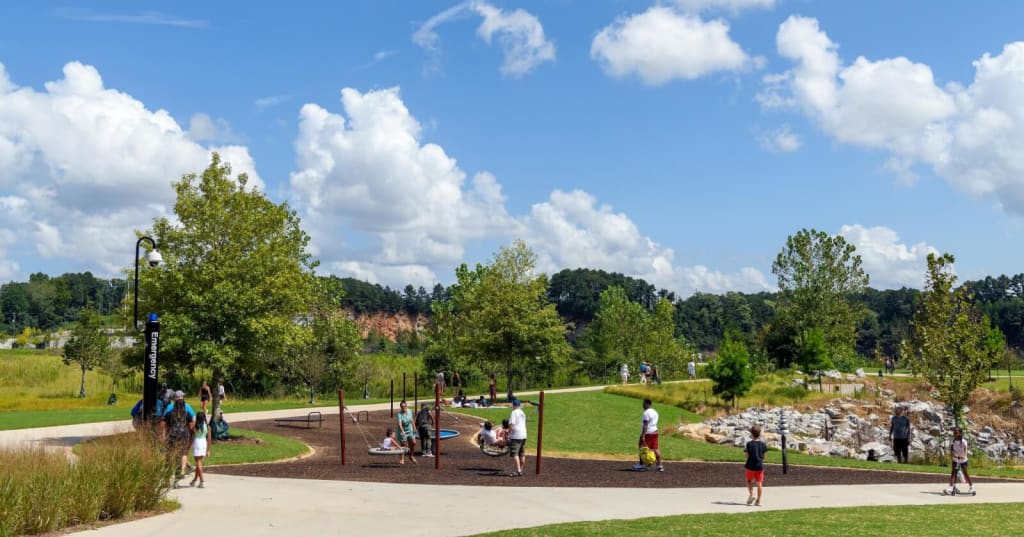 A vibrant community park bustling with activity, featuring a playground, walking paths, and lush greenery under a bright blue sky in Atlanta, Georgia.