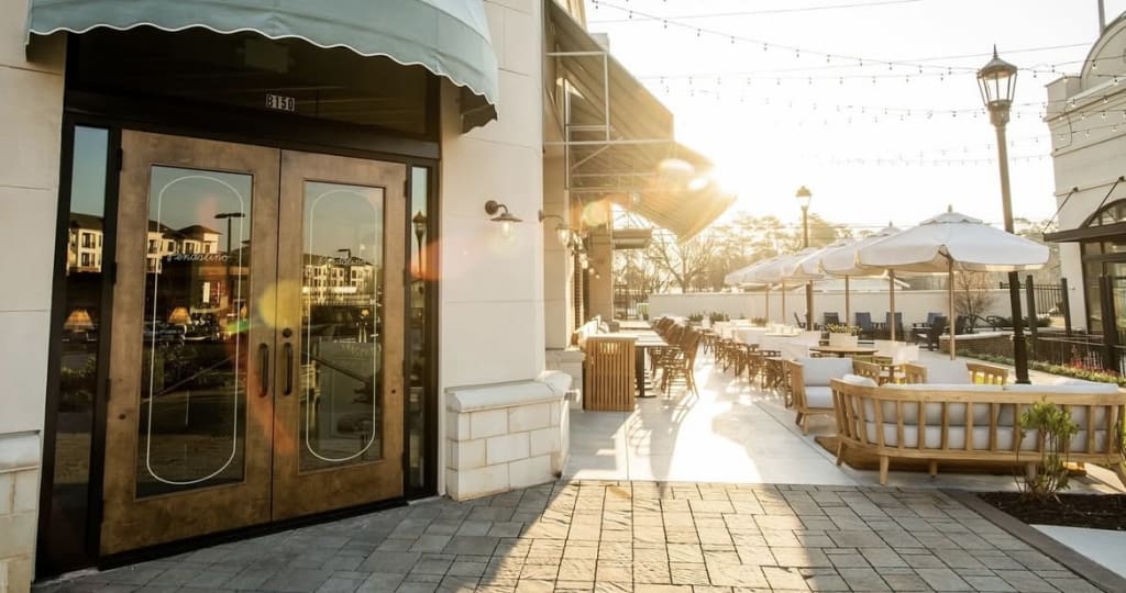 Sunlit outdoor seating area with wooden furniture and umbrellas outside a restaurant in Atlanta, Georgia.