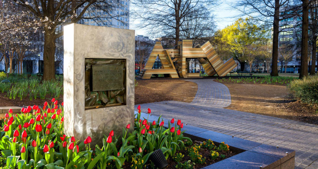 A vibrant park scene with a concrete monument, red tulips, and a wooden sculpture in the background in Atlanta, Georgia.