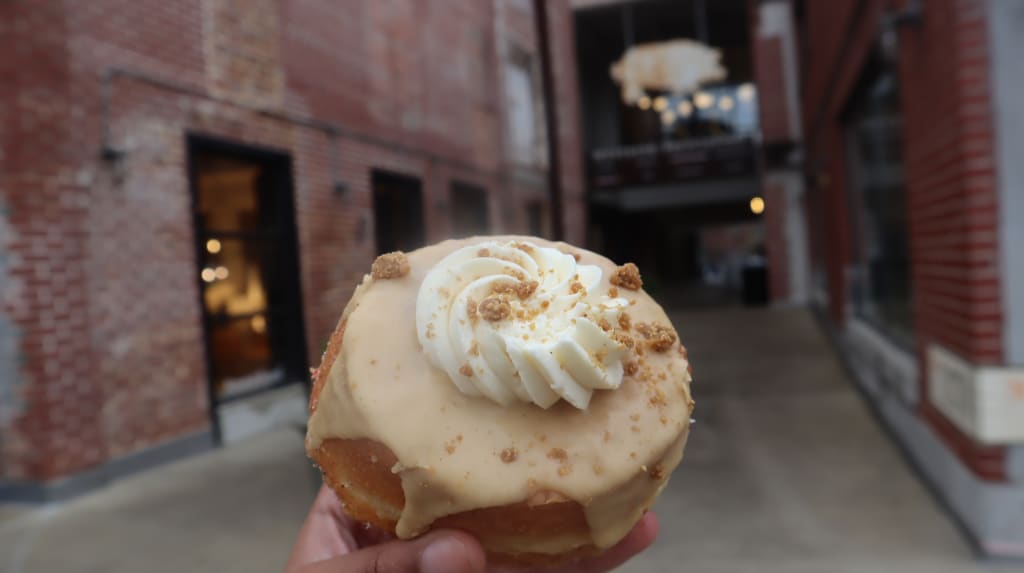A hand holds a doughnut with caramel glaze and whipped cream topping in Atlanta, Georgia.