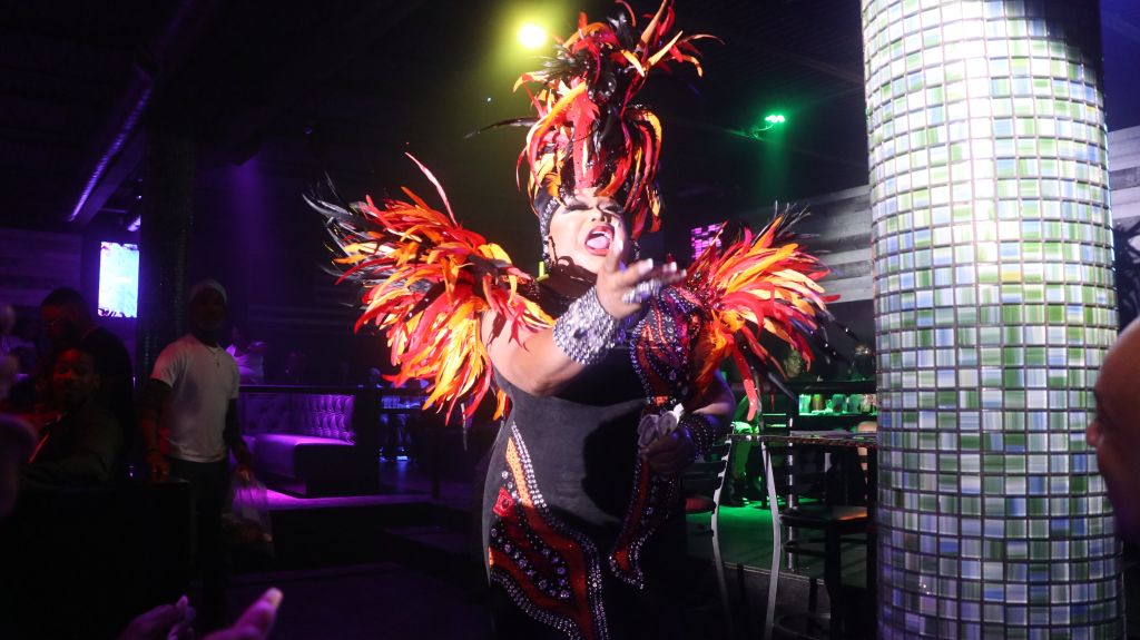 Drag queen singing wearing costume of red feathers. 