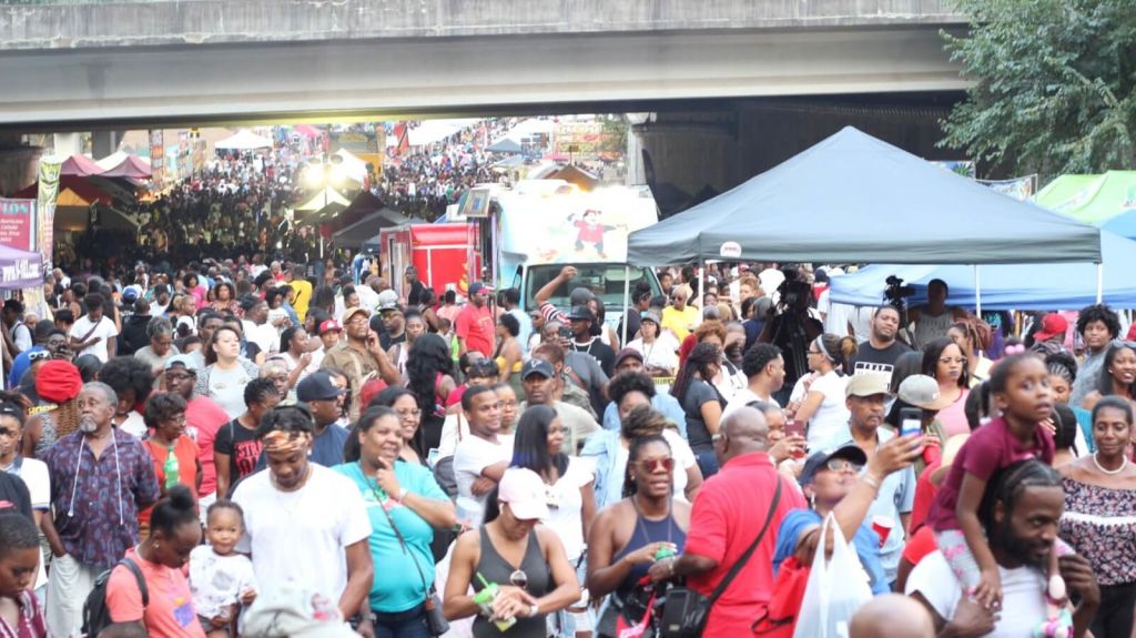 A crowded outdoor festival with people of all ages under colorful tents and umbrellas in Atlanta, Georgia.