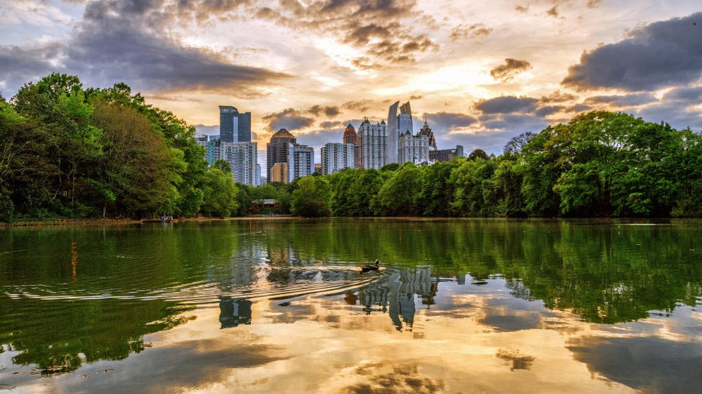 A serene lake reflects the vibrant sunset and distant city skyline in Atlanta, Georgia.