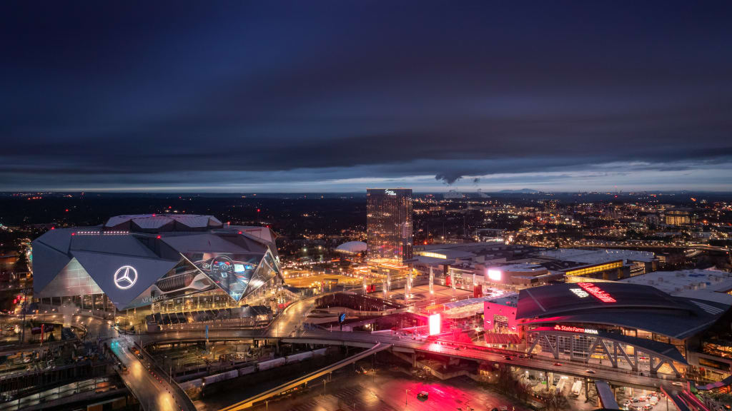A nighttime aerial view of a city skyline with illuminated buildings and a prominent Mercedes-Benz stadium in Atlanta, Georgia.