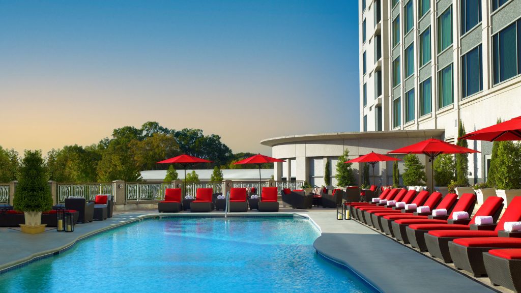 A luxurious rooftop pool area with red lounge chairs and umbrellas, adjacent to a modern building in Atlanta, Georgia.