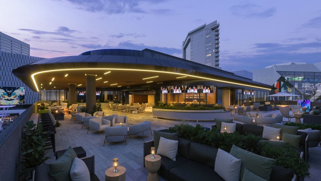 A rooftop bar with a curved, illuminated ceiling and multiple TVs, surrounded by comfortable seating and potted plants, overlooking a cityscape at dusk in Atlanta, Georgia.