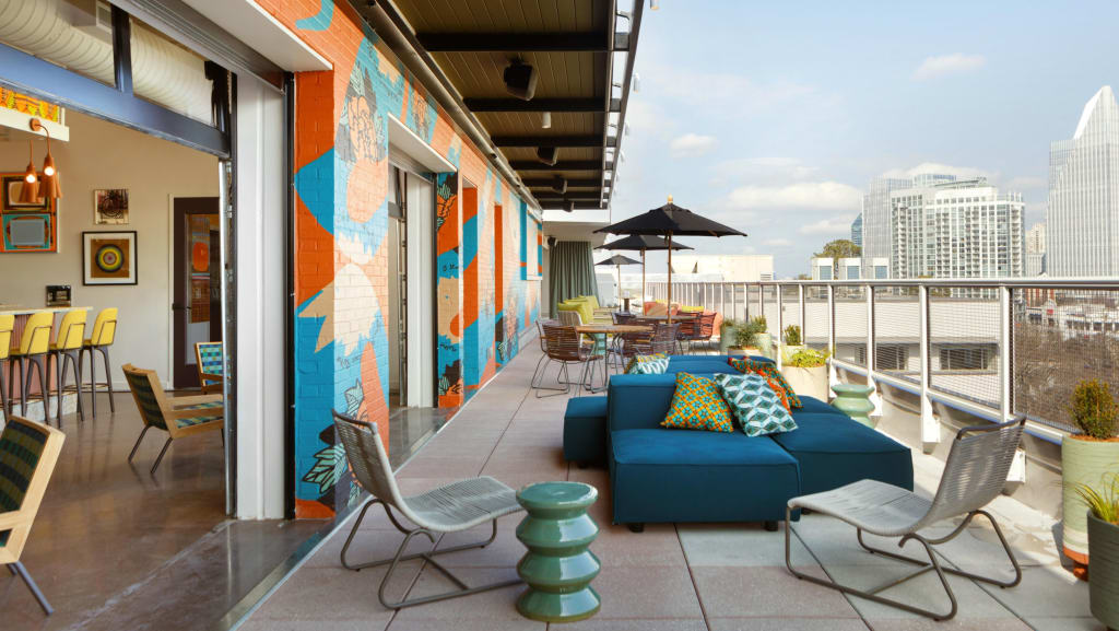 A rooftop patio with colorful furniture and murals overlooks a city skyline in Atlanta, Georgia.