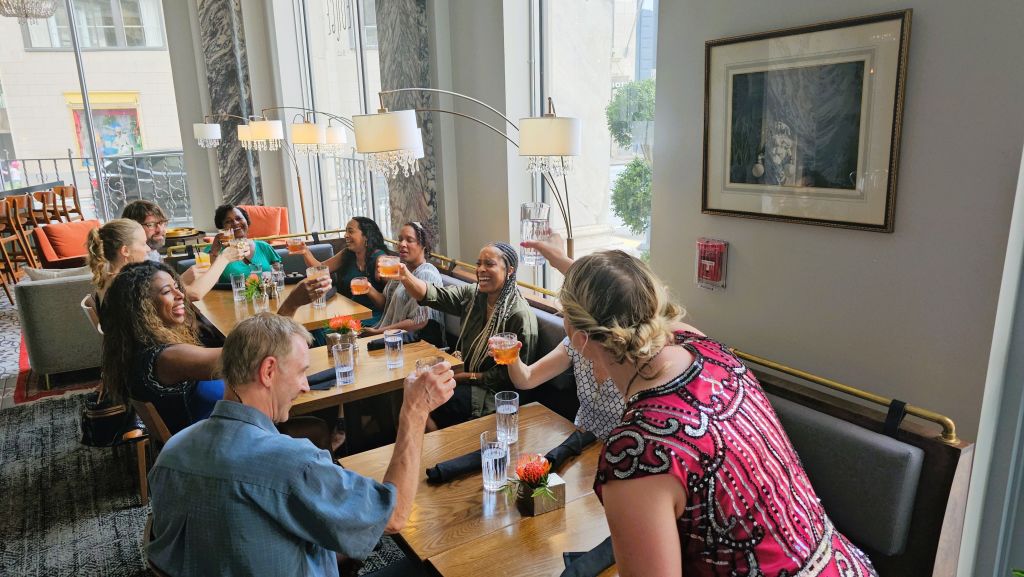 A lively group of friends enjoys a celebratory toast at a stylish restaurant with large windows and elegant decor in Atlanta, Georgia.