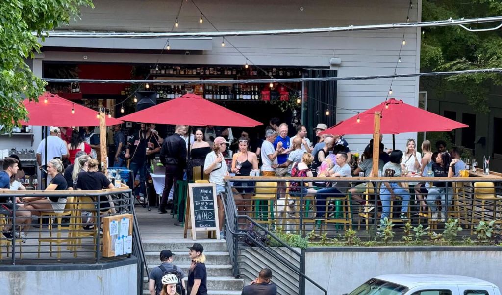 A bustling outdoor restaurant with red umbrellas and string lights, filled with people enjoying drinks and meals at tables and the bar in Atlanta, Georgia.