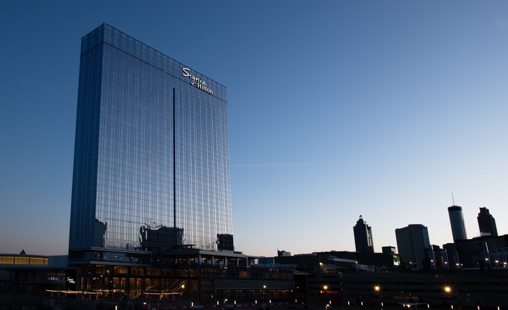 A tall, reflective glass skyscraper stands prominently against a clear blue sky at dusk in Atlanta, Georgia.