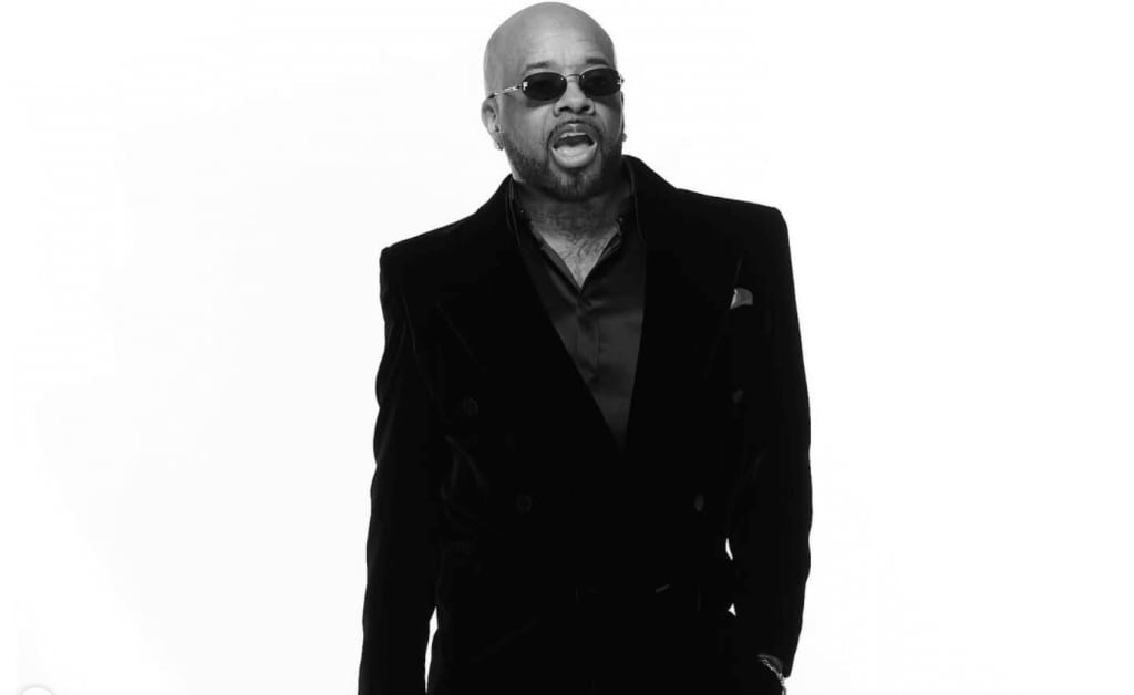 A bald man in a black suit and sunglasses stands confidently against a white background in Atlanta, Georgia.