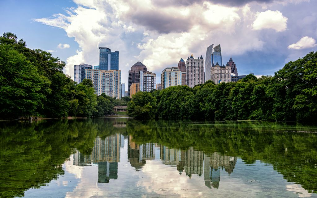 Midtown Atlanta skyline framed by lush green trees under a cloudy sky from Piedmont Park