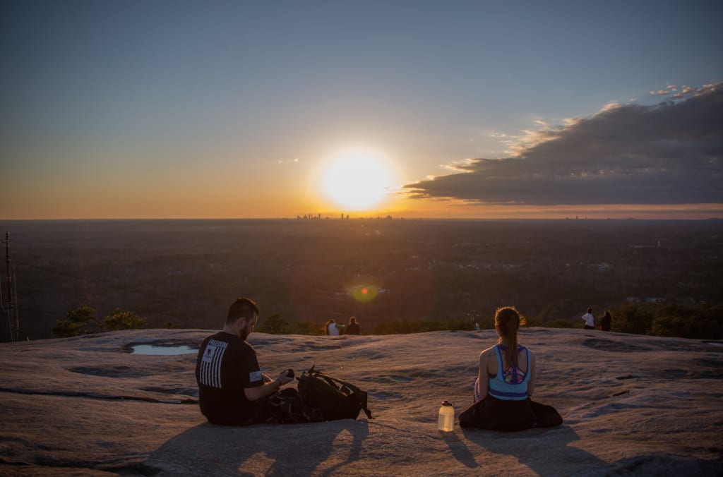 Two people sit on a rocky outcrop at sunset, overlooking a vast landscape in Atlanta, Georgia.