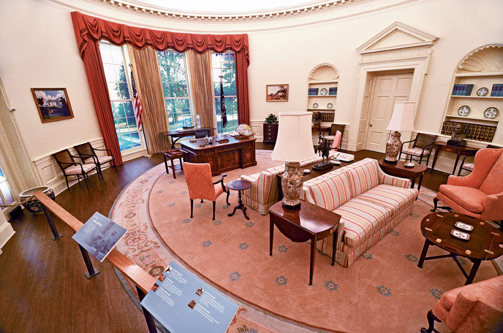 Elegant oval room with striped sofa, armchairs, and desk near large windows with red drapes in Atlanta, Georgia.