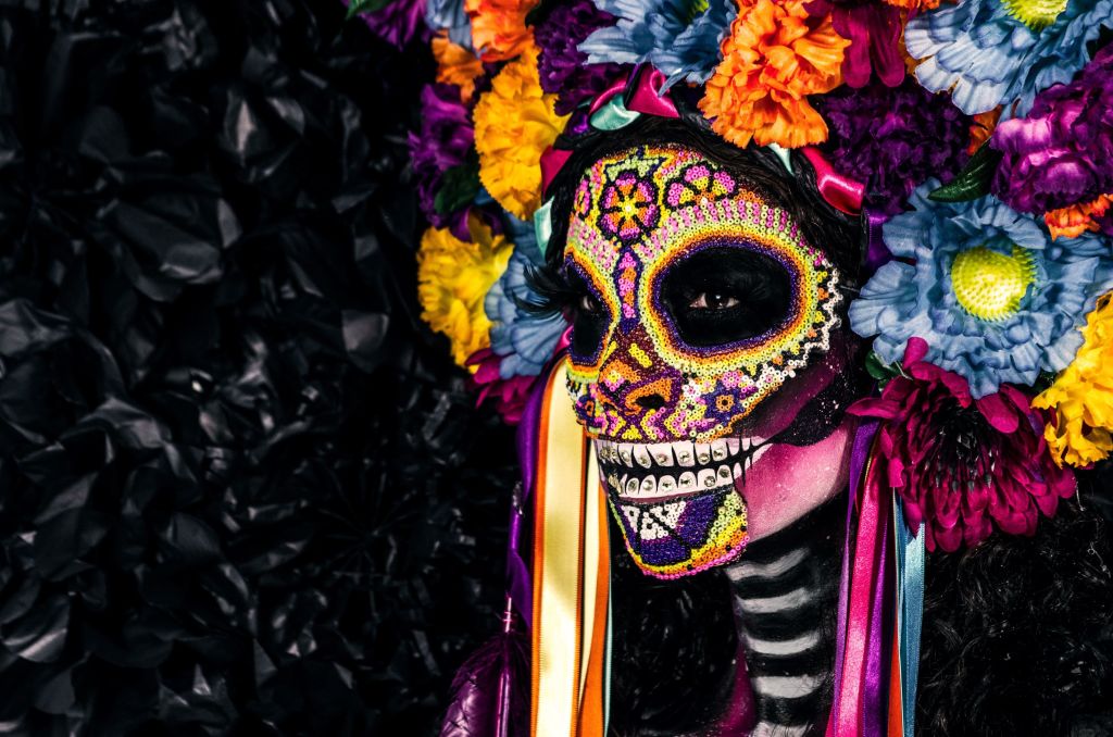 A person wearing a colorful sugar skull mask adorned with vibrant flowers and ribbons in Atlanta, Georgia.