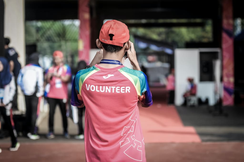 A volunteer wearing a red cap and shirt with 'VOLUNTEER' on the back stands on a red carpet in Atlanta, Georgia.