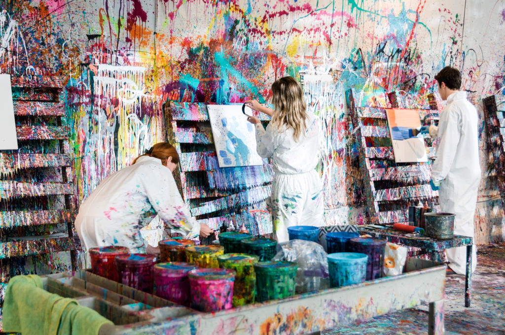 Three artists in white coveralls paint a vibrant, colorful mural on a wall in Atlanta, Georgia.