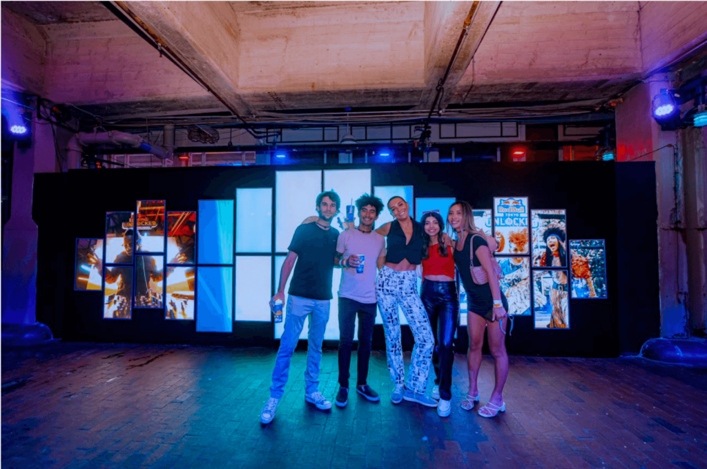Five young adults pose together in a dimly lit room with colorful posters and lights in Atlanta, Georgia.