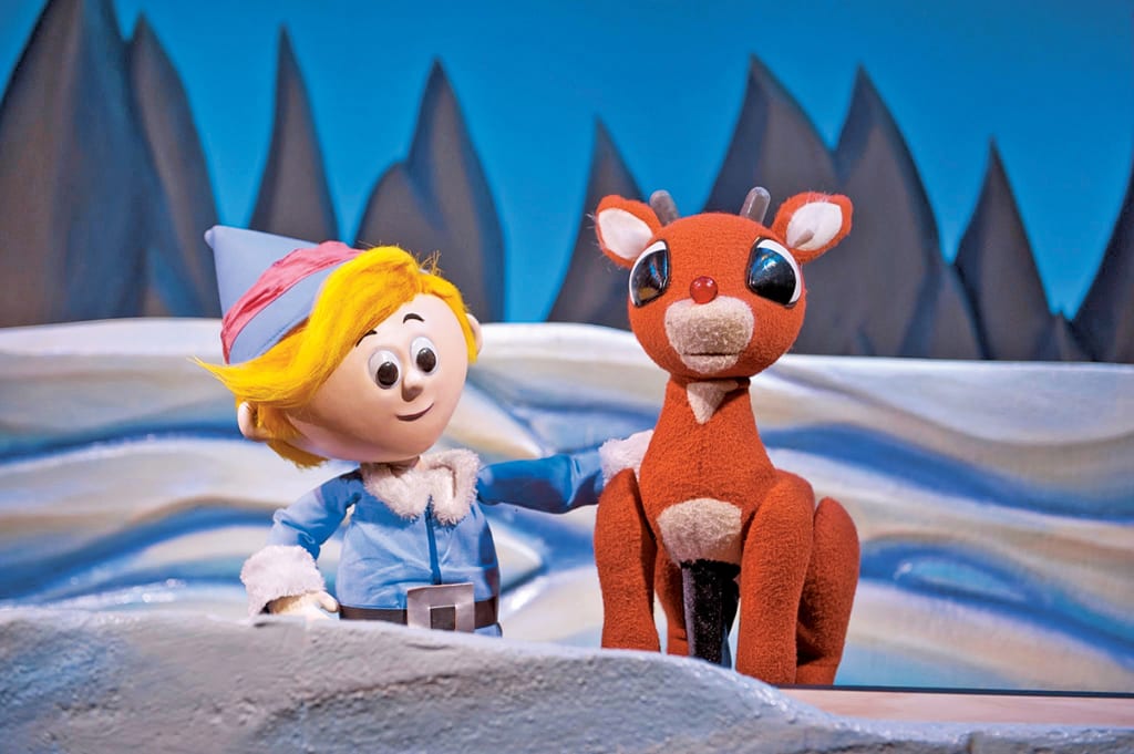 An elf in blue attire and a red-nosed reindeer stand together on a snowy stage in Atlanta, Georgia.