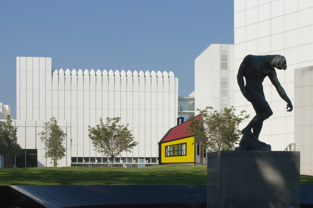A bronze statue of a muscular man stands on a pedestal in front of modern buildings in Atlanta, Georgia.
