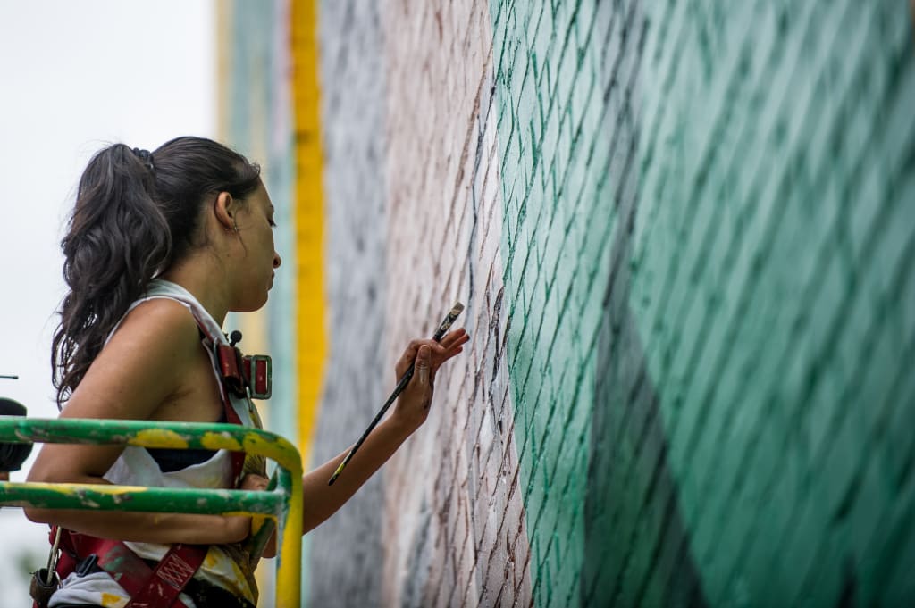 A woman in a harness paints a colorful mural on a tall wall in Atlanta, Georgia.