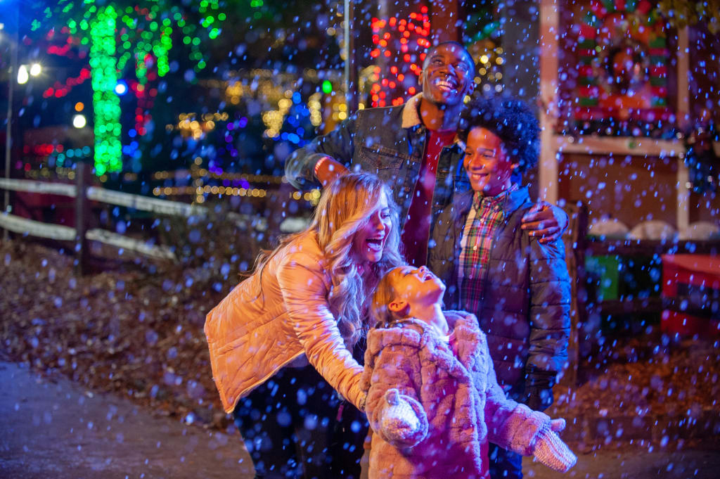 A joyful family of four plays in the snow, surrounded by festive holiday lights in Atlanta, Georgia.