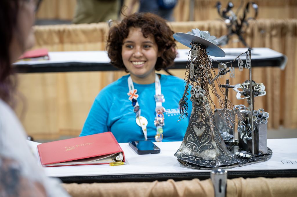 A woman with curly hair smiles while sitting at a table with a unique metal sculpture and a red binder in Atlanta, Georgia.