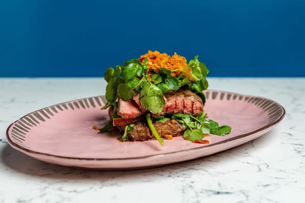 A beautifully plated dish featuring seared steak slices, greens, and orange garnish on a pink plate in Atlanta, Georgia.