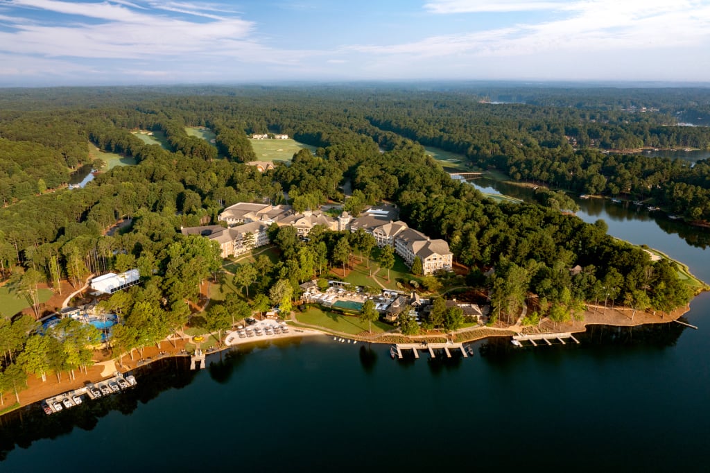 Aerial view of a resort with multiple buildings, golf courses, and a marina on a lake surrounded by dense forest in Atlanta, Georgia.