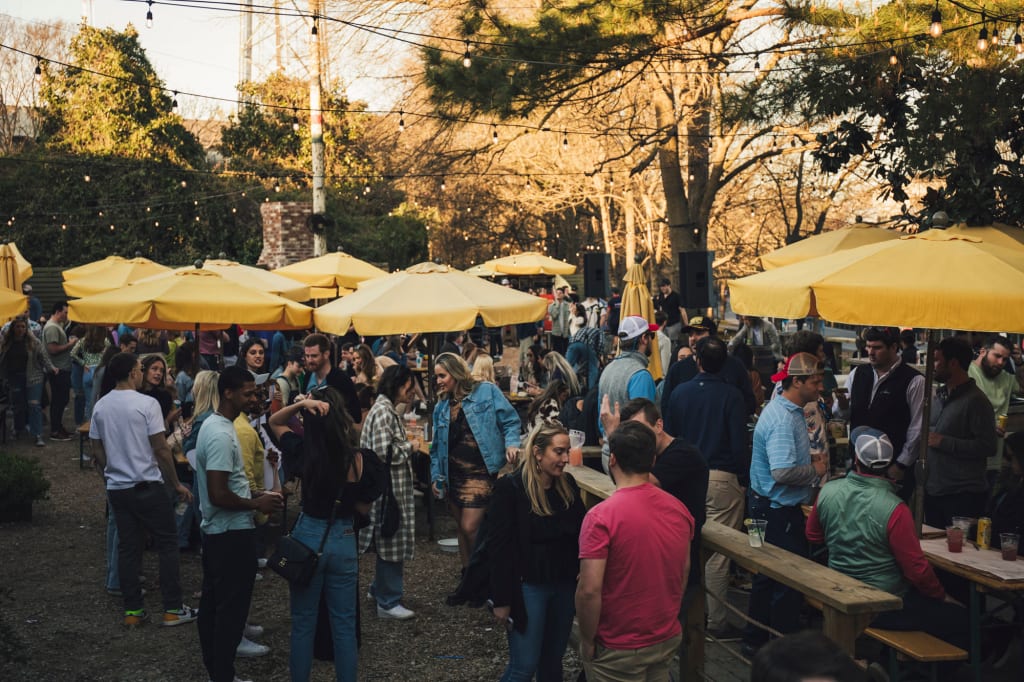 Crowded outdoor event with people socializing under yellow umbrellas and string lights in Atlanta, Georgia.