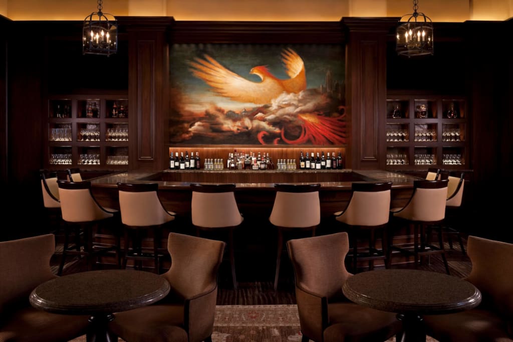 An opulent bar with a large mural of a phoenix behind the counter, surrounded by shelves of liquor and wine glasses in Atlanta, Georgia.