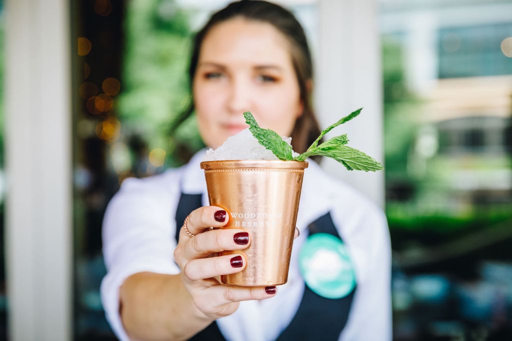 A woman in a white shirt and black vest holds a copper mug with a mint sprig and ice in Atlanta, Georgia.