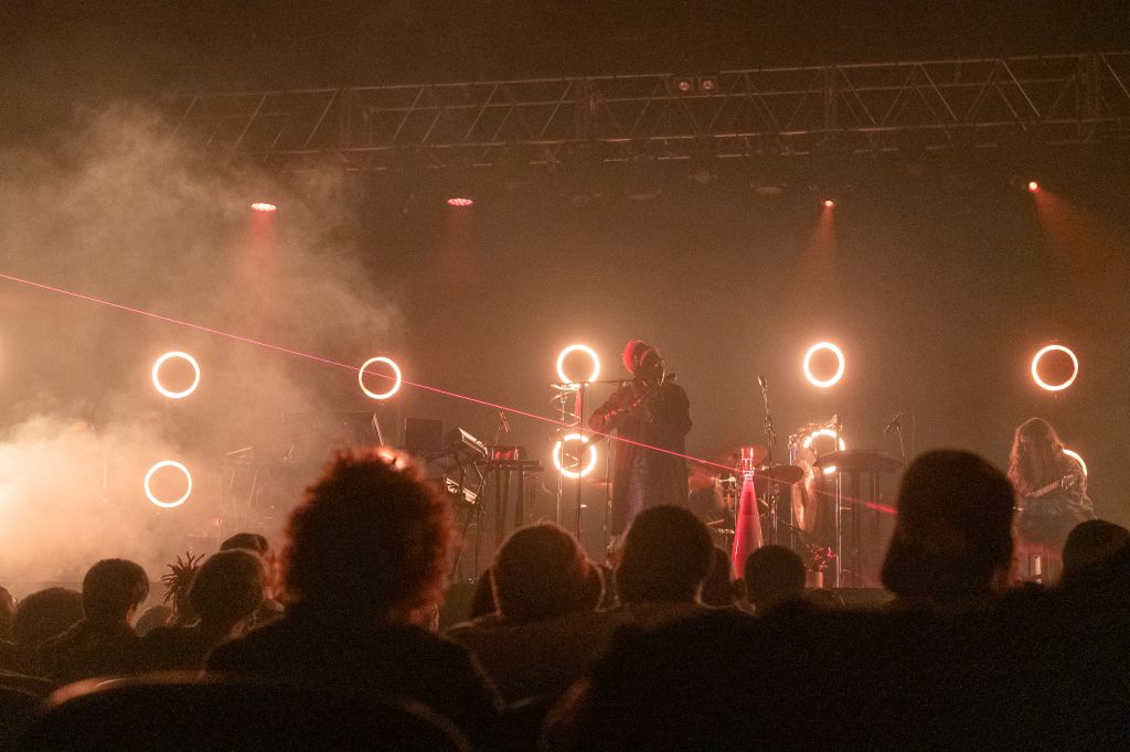 A musician performs on stage with glowing rings and smoke effects, viewed from the audience in Atlanta, Georgia.