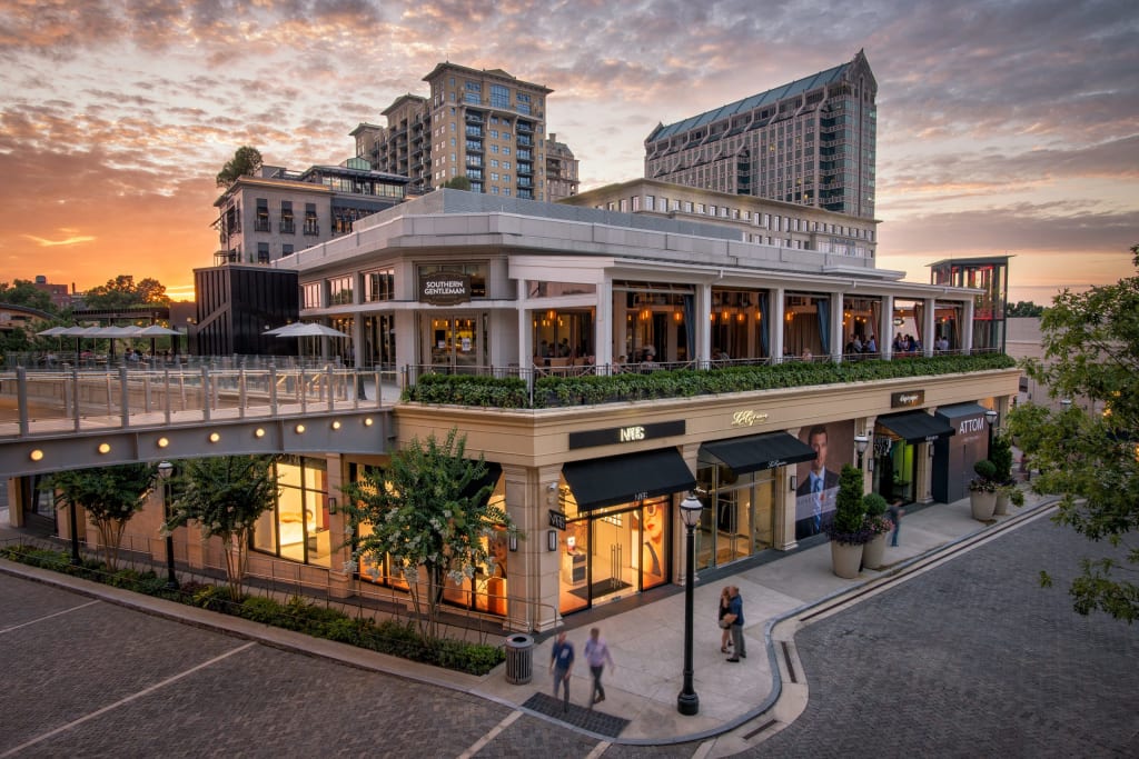 Modern shopping center with restaurants and stores at dusk, featuring a rooftop garden and pedestrians in Atlanta, Georgia.