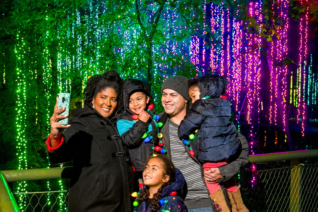 A family of five takes a selfie in a magical forest illuminated with colorful Christmas lights in Atlanta, Georgia.