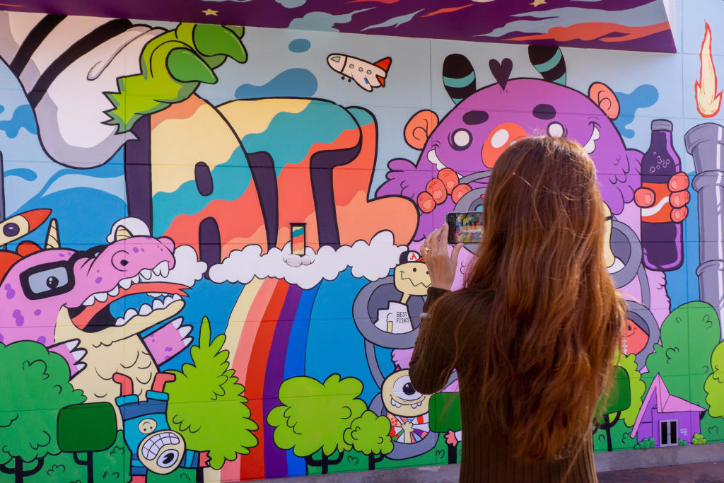 A woman with long hair is taking a photo of a colorful mural featuring cartoon characters and a rainbow in Atlanta, Georgia.