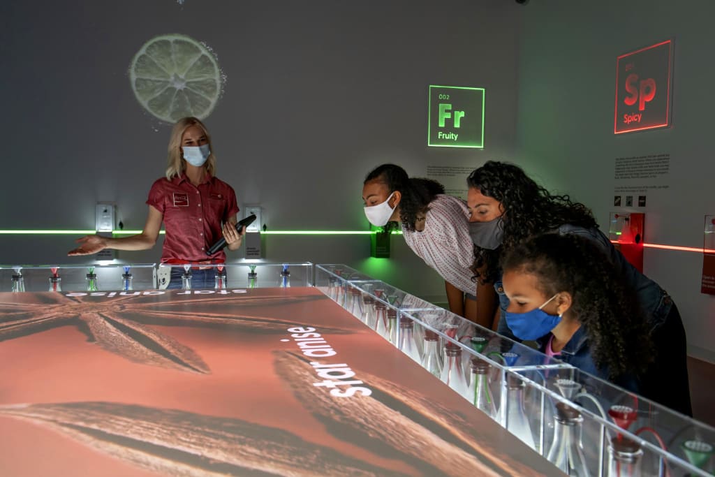 A woman and three children, all wearing masks, are interacting with a large, colorful, touch-sensitive display table in Atlanta, Georgia.