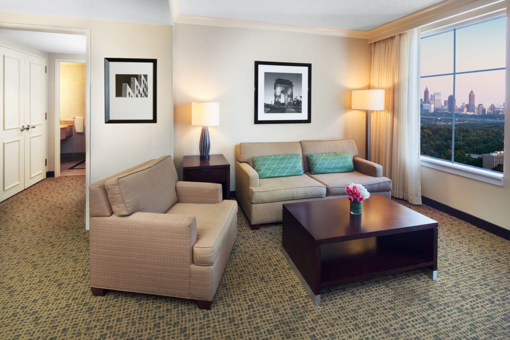 Modern hotel room with beige sofa, armchair, coffee table, and city skyline view in Atlanta, Georgia.