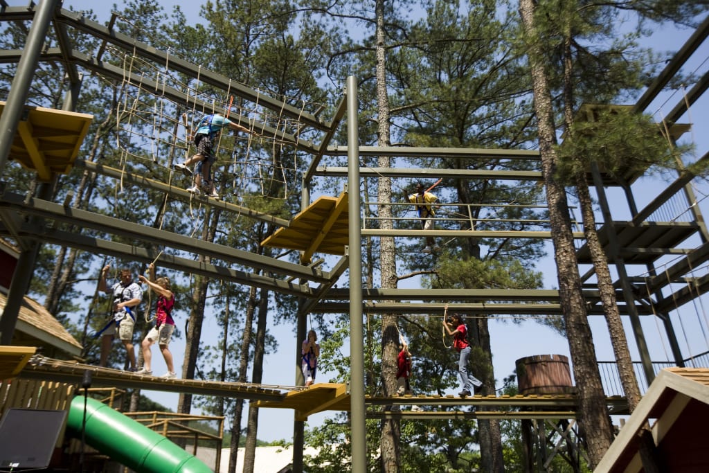 People navigate an aerial ropes course with bridges and climbing elements among tall trees in Atlanta, Georgia.