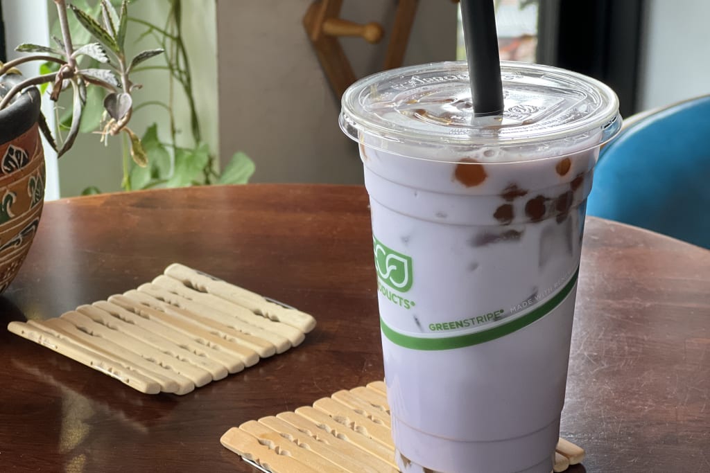 A purple bubble tea with tapioca pearls sits on a wooden coaster next to a plant in Atlanta, Georgia.