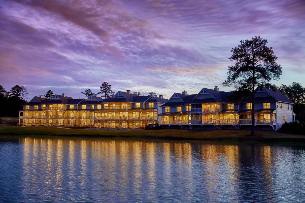A serene lakeside resort with multiple buildings illuminated at dusk, reflecting on the calm water in Atlanta, Georgia.