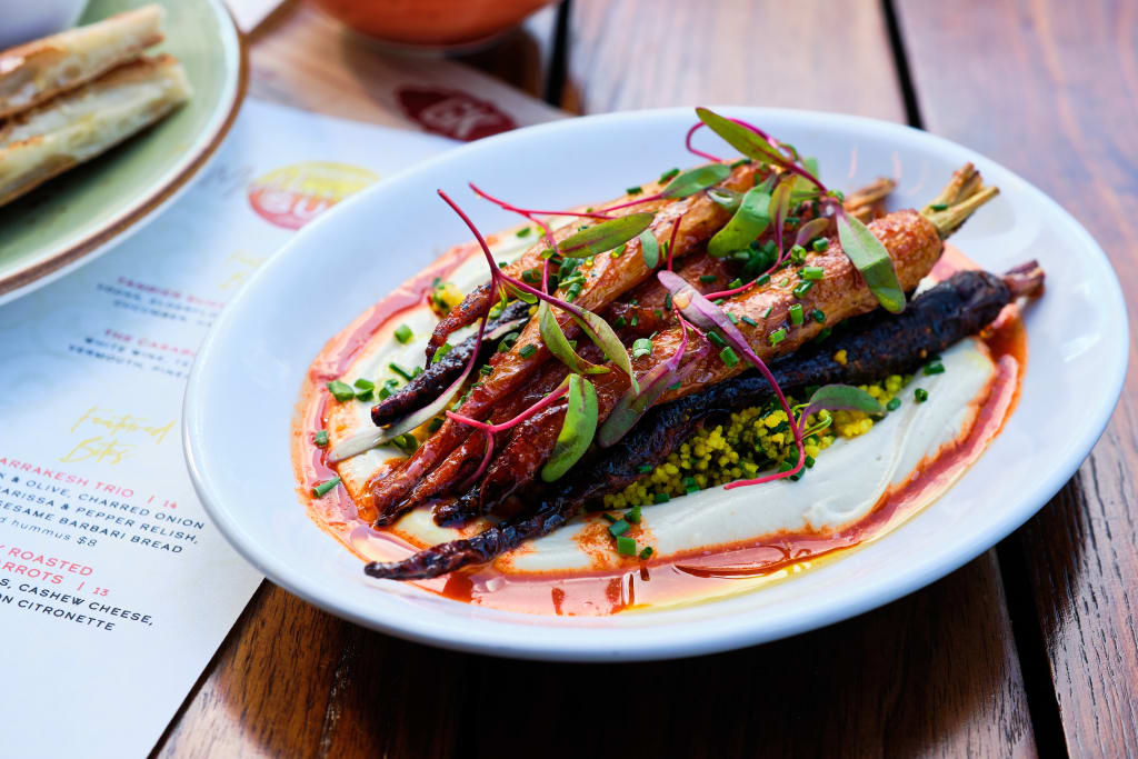 A white plate holds roasted carrots and dark greens in a creamy sauce, garnished with herbs in Atlanta, Georgia.
