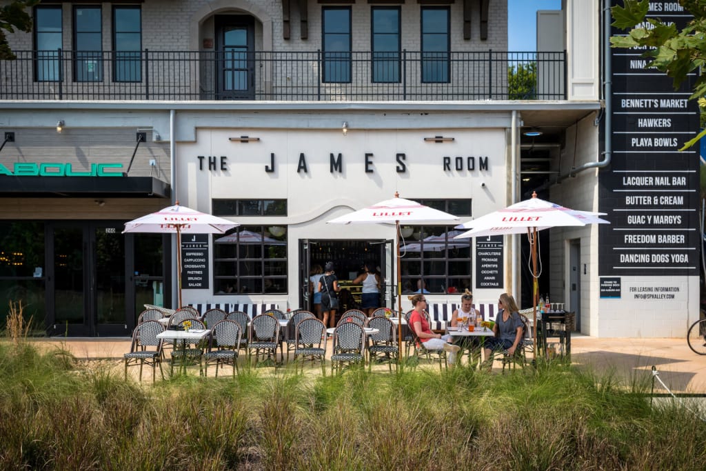 Outdoor seating area with umbrellas and tables in front of a restaurant called The James Room in Atlanta, Georgia.