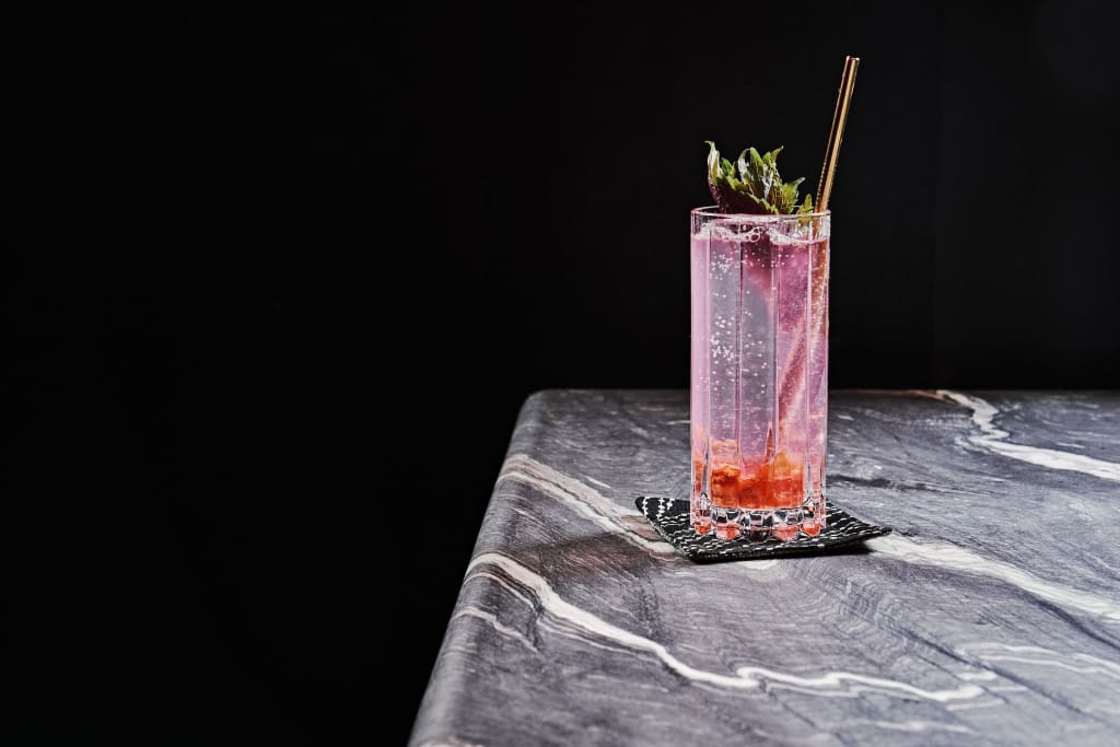 A tall glass of pink sparkling drink with a strawberry and mint garnish on a dark marble table in Atlanta, Georgia.
