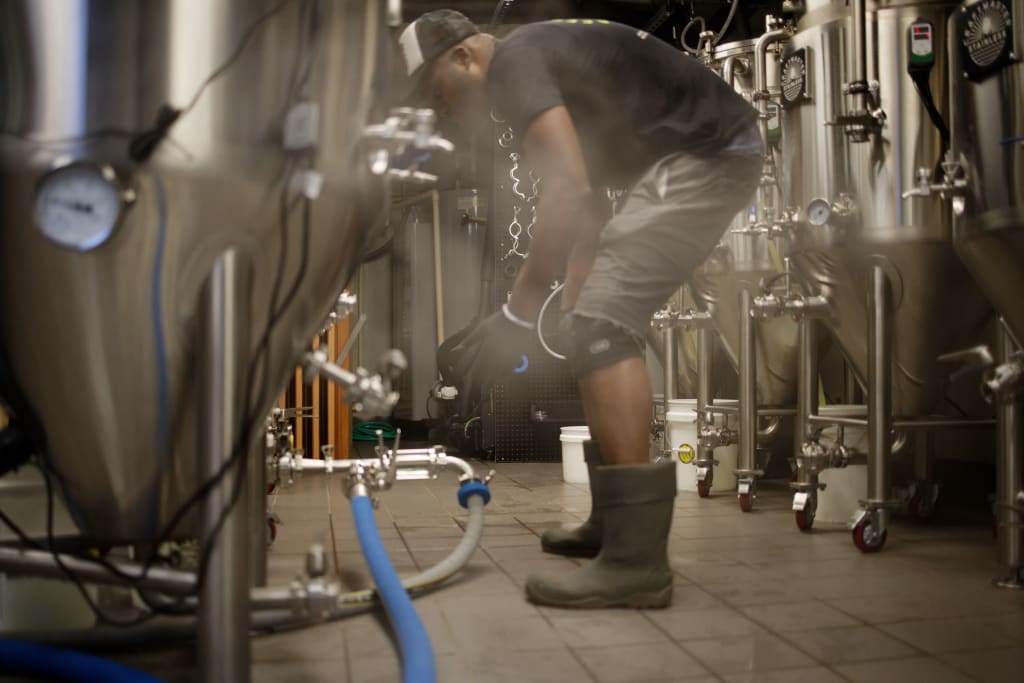 A worker in a brewery adjusts equipment while wearing protective gear in Atlanta, Georgia.