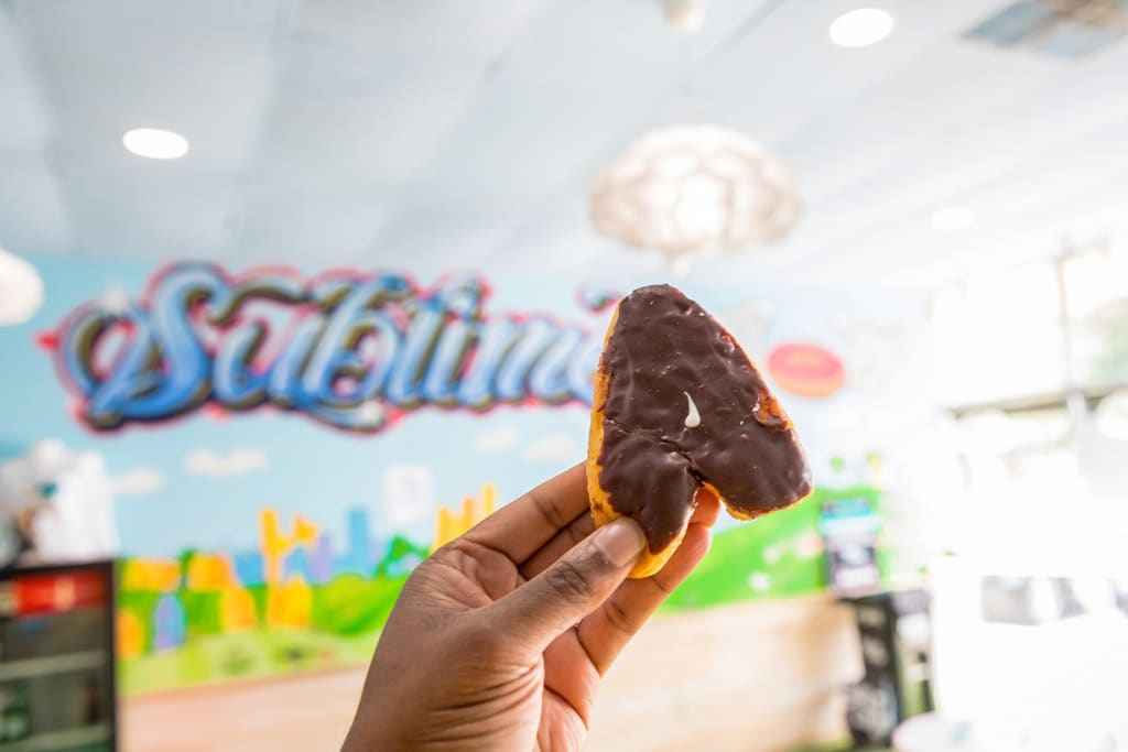 A hand holds a chocolate-covered pastry shaped like a heart against a colorful mural in Atlanta, Georgia.