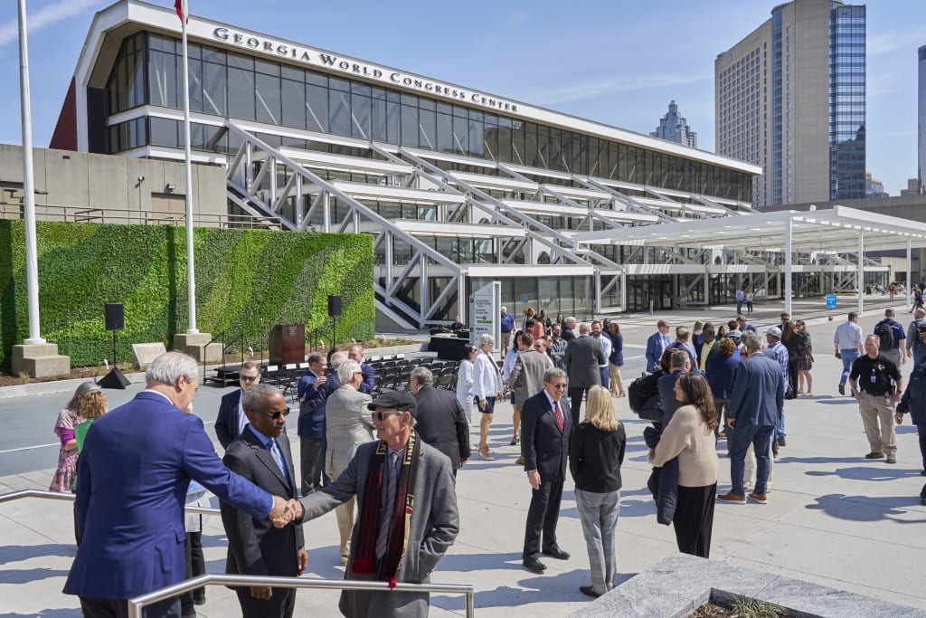 Crowd of people in business attire gathered outside modern building with green wall in Atlanta, Georgia.