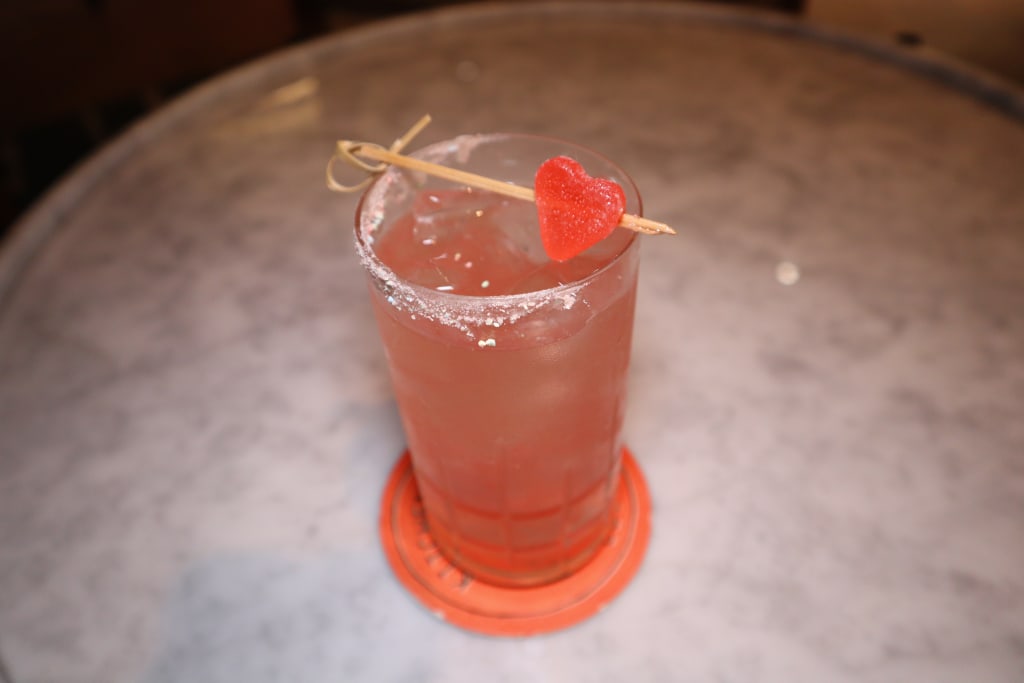 A vibrant pink cocktail garnished with a heart-shaped candy sits on a coaster in Atlanta, Georgia.